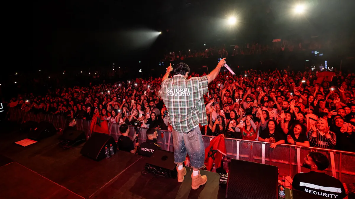 DYSTINCT on stage, seen from behind, facing a packed crowd in red light